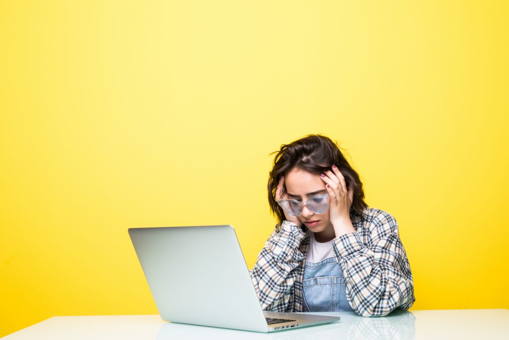 a woman sitting in fornt of a laptop putting her hands on the sides of her head